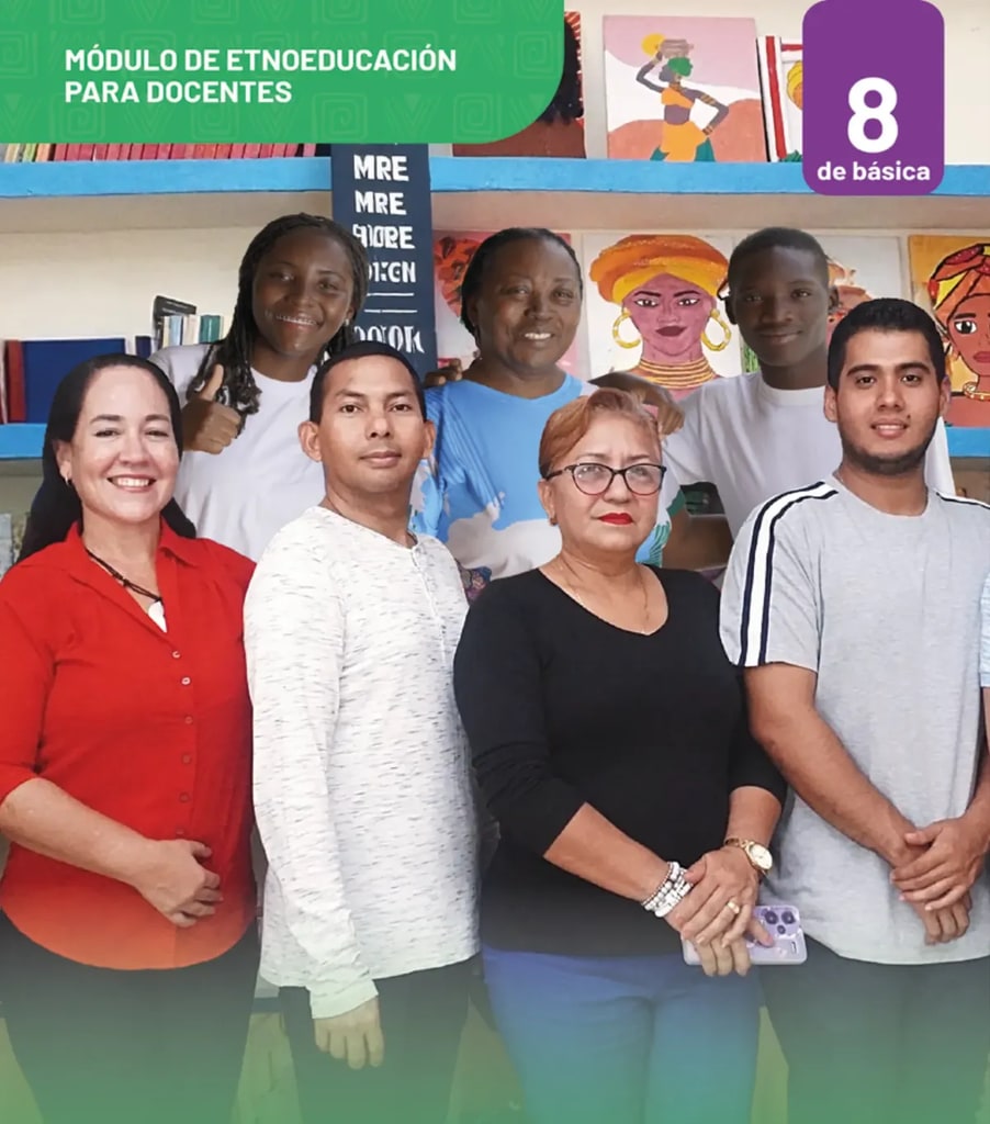Fotografía grupal de siete personas (docentes y estudiantes afroecuatorianos) sonrientes en un espacio educativo con estanterías de libros y retratos artísticos de mujeres afrodescendientes al fondo.