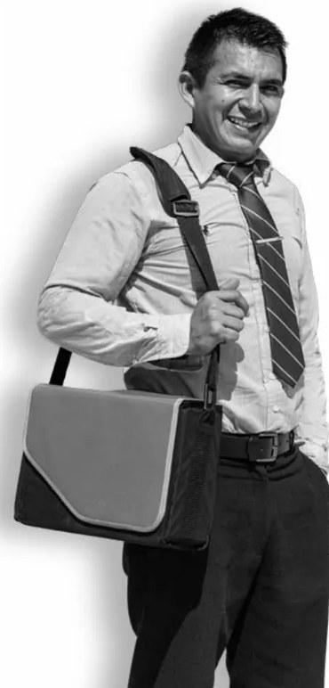 Fotografía en blanco y negro de un hombre adulto sonriente, vestido con camisa, corbata y maletín, en actitud de director o docente listo para iniciar el año escolar.