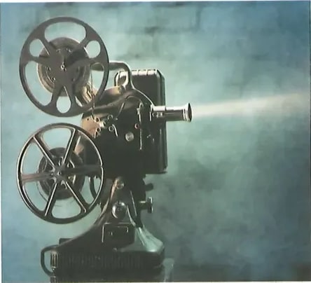 Fotografía de un proyector de cine antiguo con carretes de película, proyectando un haz de luz en ambiente oscuro. Imagen representativa del tema de la proyección cinematográfica. Crédito: Shutterstock (2020) 92369284.