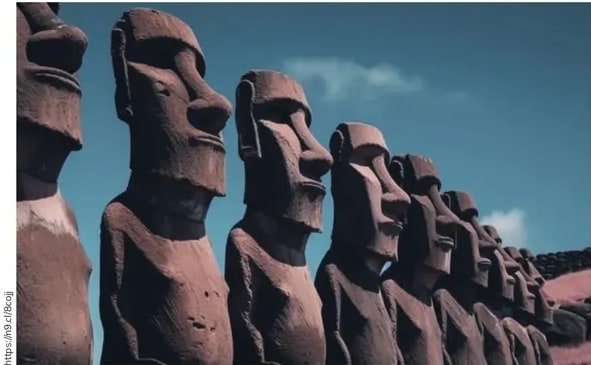 Fotografía de los moai de la Isla de Pascua alineados, vistos en perspectiva contra cielo azul.