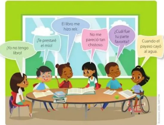 Escena con seis niños alrededor de una mesa con libros, conversando; uno de ellos usa silla de ruedas.