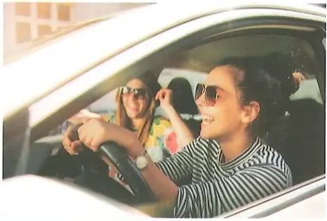 Fotografía de jóvenes dentro de un automóvil. La conductora lleva lentes de sol y sonríe; se ve a otro pasajero al fondo. Imagen para el ejercicio 7, segundo recuadro de escritura (amarillo). Crédito: Shutterstock (2020) 483328555.