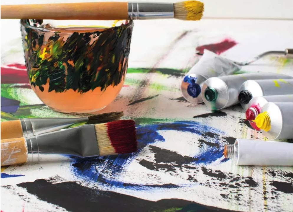 Fotografía de tubos de pintura al óleo, pinceles y paleta con pintura, simbolizando el oficio del pintor.