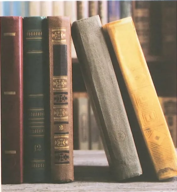 Fotografía de varios libros de distintos colores (verdes, rojos, azules, amarillos, marrones) colocados en posición vertical en una estantería, vistos desde el canto. La imagen ilustra el concepto de libros de consulta, enciclopedias y libros escolares como ejemplos de textos expositivos. Crédito: Shutterstock (2020) 580981603.