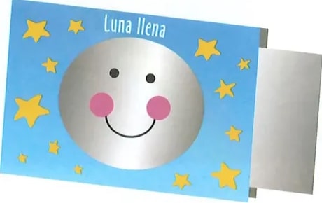 Tarjeta ilustrativa de la luna llena: círculo gris claro completo con cara sonriente (ojos punteados y mejillas rosadas). Fondo azul celeste con estrellas amarillas de cinco puntas. Etiqueta superior: 'Luna llena'. La tarjeta tiene un efecto de página doblada en la esquina derecha.