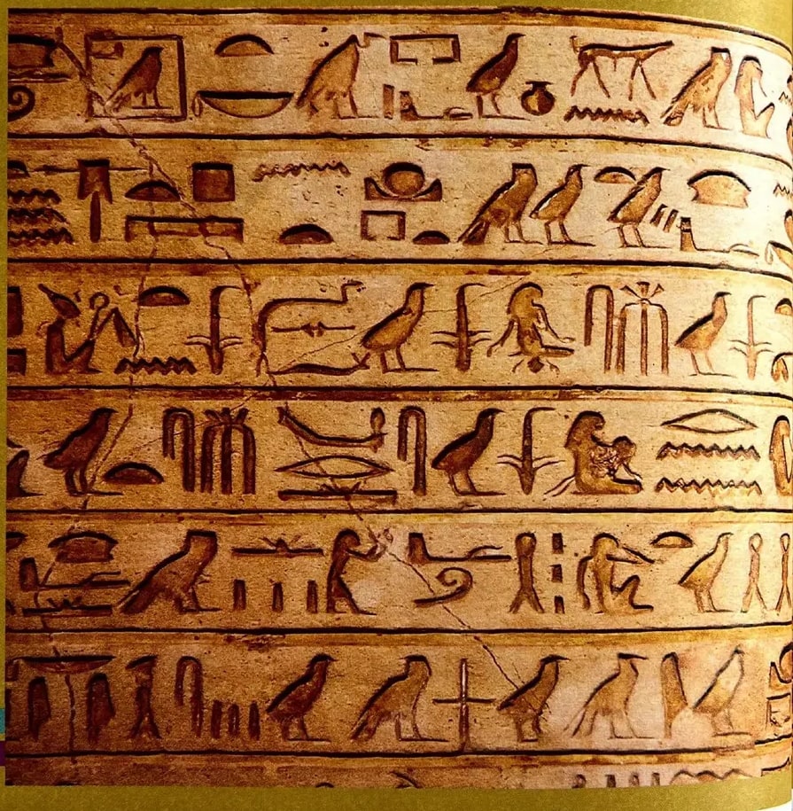 Fotografía a gran tamaño de un muro con jeroglíficos egipcios tallados; aves, figuras humanas y símbolos esculpidos en piedra evocan los orígenes de la escritura y el vínculo entre lengua y sociedad.