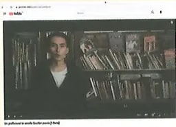 Miniatura de video en el panel Competencia digital: imagen de una persona frente a estantes de libros (aspecto de librería o biblioteca), posiblemente un escritor o profesor que enseña a escribir poesía. Se usa como thumbnail del enlace lynk.ec/8y33.